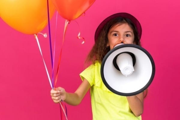 surprised little caucasian girl with purple party hat holding helium balloons speaking into loud speaker isolated pink wall with copy space 141793 108370