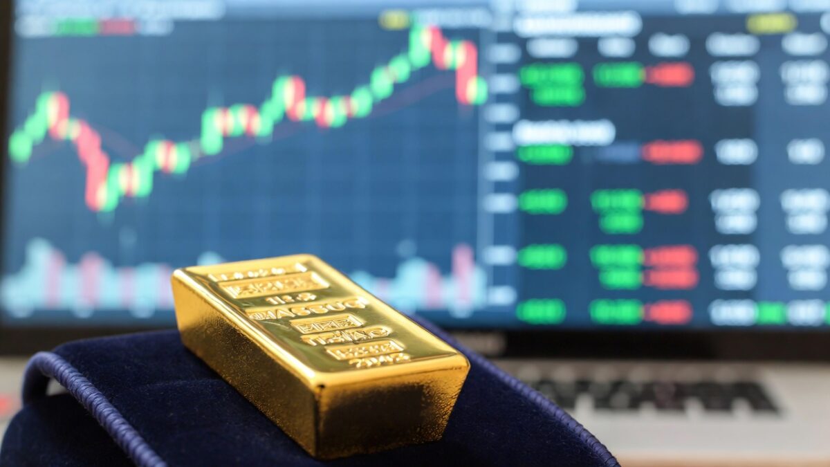 Lingouri de aur de 24 de carate și monede de investiții așezate pe un fundal cu grafice economice.