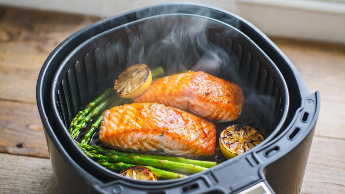 Somon și legume crocante aburinde într-un coș de airfryer modern pe un blat de bucătărie.